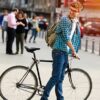 man standing in front of steps with bike looking back with headphones and backpack on